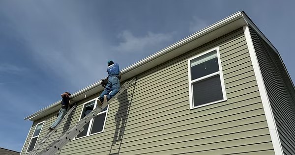 Flow-Masters crew installing seamless gutters from ladders on a two-story home
